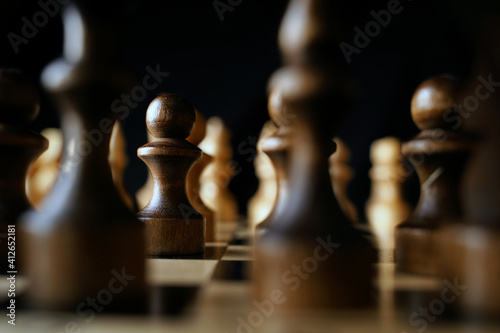 Close up of black chess pieces on board. Two rows of wooden figures on chessboard on black background. Concept of intelligent, logical and strategic game.