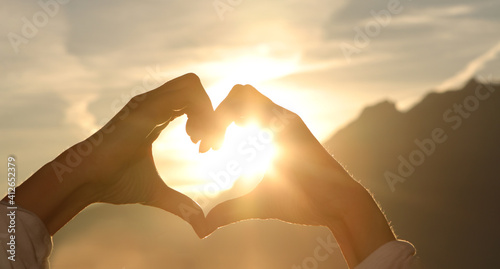 The hands of women and men are the heart shape with the sun light passing through the hands