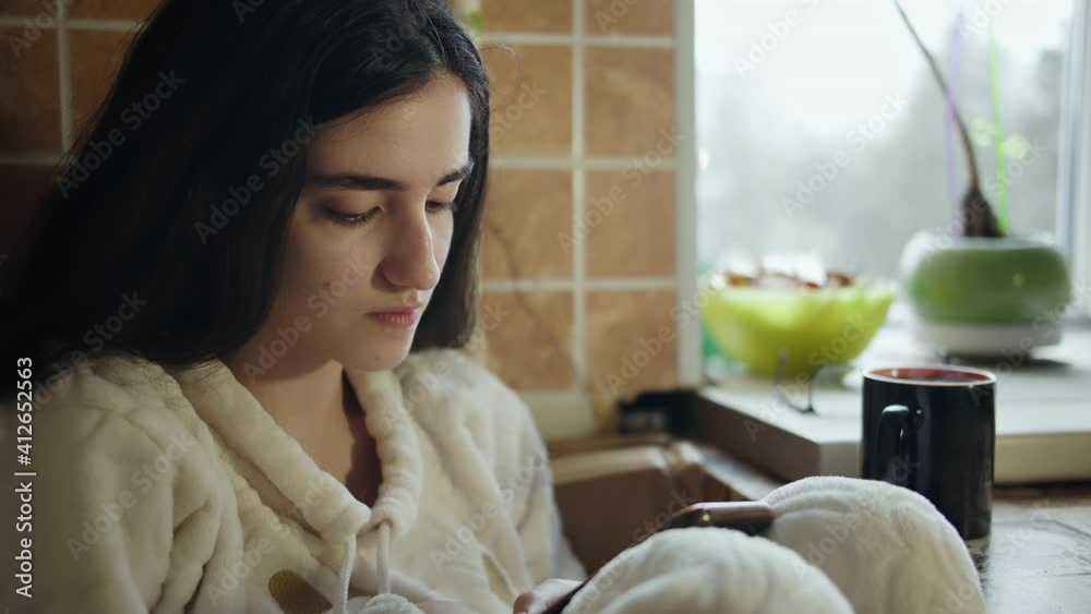 Teen girl writes a message on a mobile phone, sits at home at the table, camera tracking Teen girl writes a message on a mobile phone, sits at home at the table, camera tracking