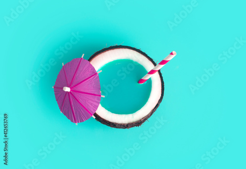 Tropical summer and vacation minimal concept. Coconut on a blue background with a cocktail straw. Vacation, travel, beach idea.