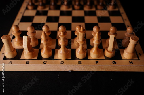 White wooden pieces on a chessboard. A chessboard set up during a game on a black background