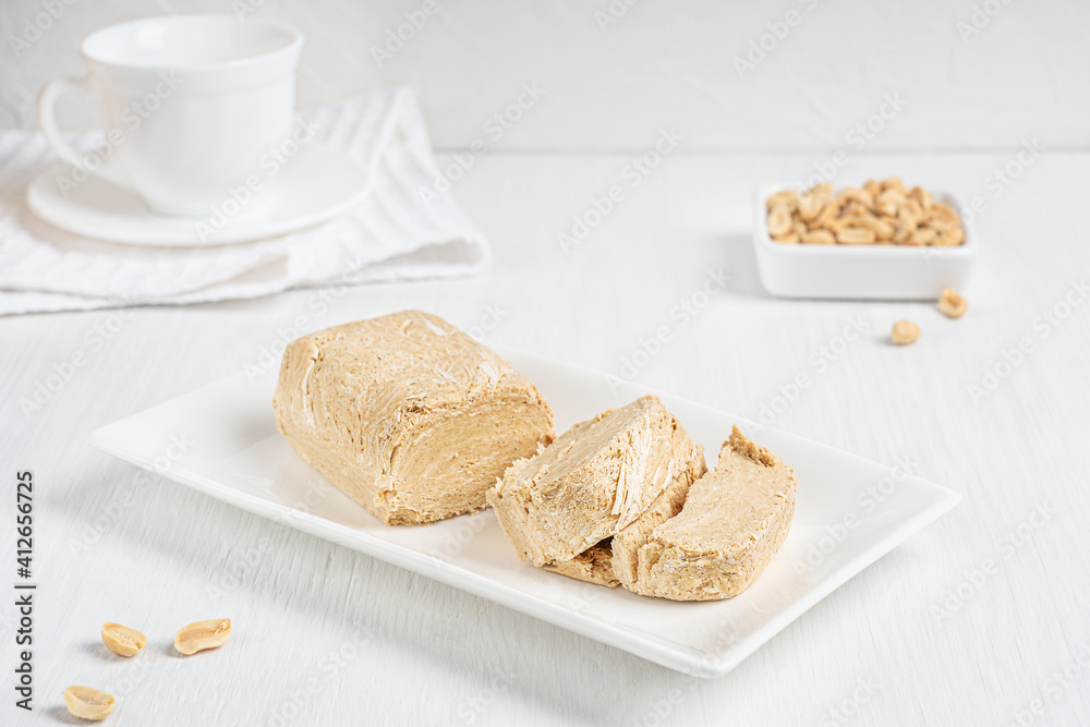 Halva, also halvah or halwa West Asia local dessert made of peanut oily seeds grinded to a paste and mixed with sugar syrup served on plate on white wooden table at kitchen at breakfast. Horizontal