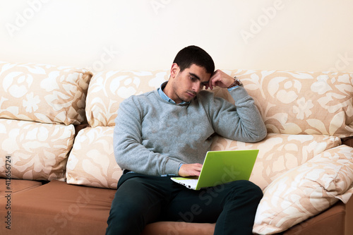 young man gets bored looking at a small laptop on the sofa at home