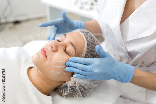 Foto Cosmetologist massage movements apply a cleansing mask on the face of the patien