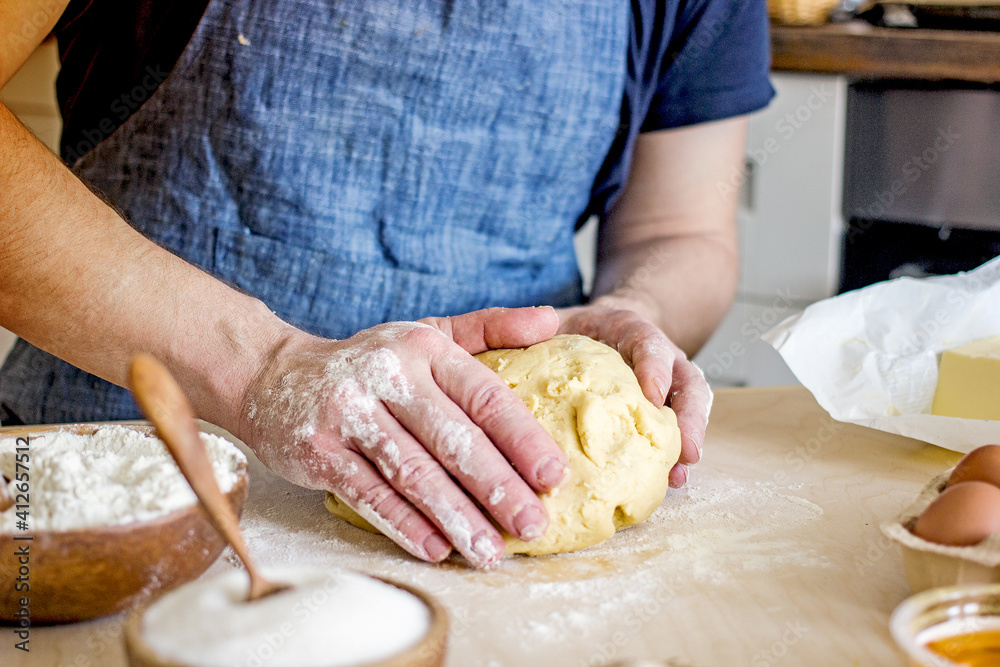A faceless man in an apron in his kitchen at the kitchen table kneads bread dough with his hands. Home authentic hobby, home baker. Baking bread with your own hands A faceless man in an apron in his kitchen at the kitchen table kneads bread dough with his hands. Home authentic hobby, home baker. Baking bread with your own hands