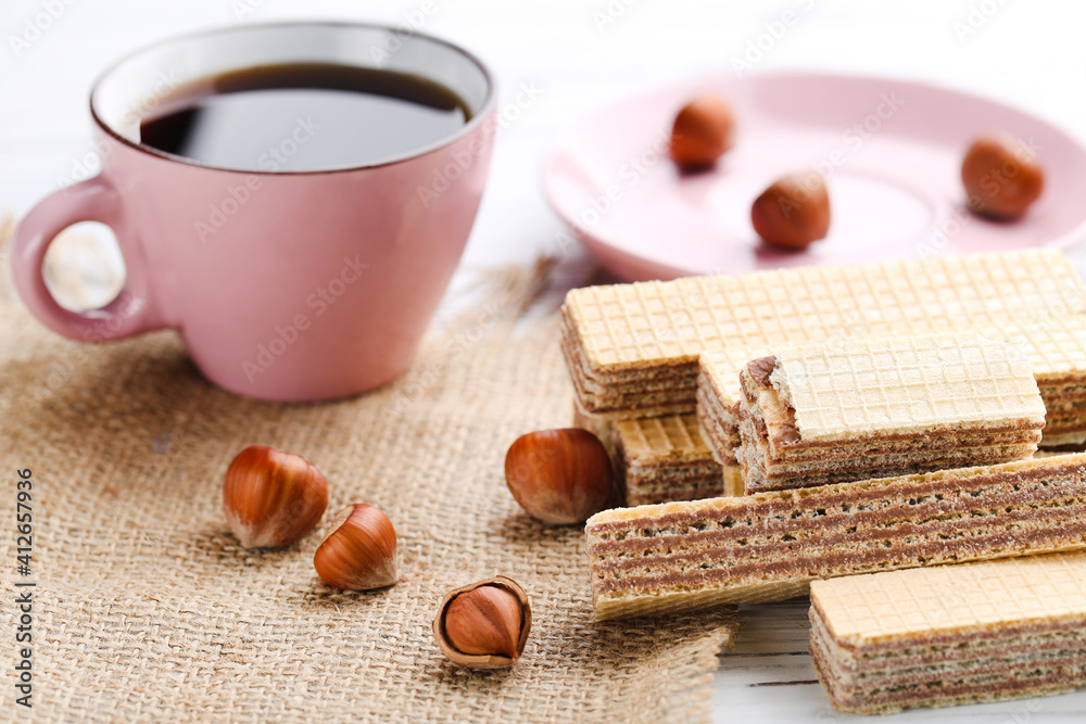 Wafer sticks with hazelnuts and cup of coffee on white wooden background