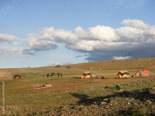 Horse trekking in Mongolia. Camping tents and horses in Mongolian landscape. Wild campingsite. Dramatic sky.