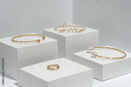 Photo Golden bracelets and ring on white cubes eith copy space