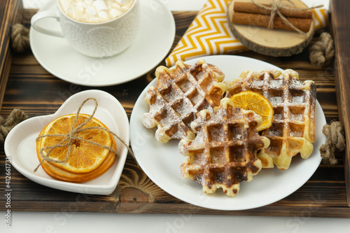 Early breakfast coffee with marshmallows and a stick of cinnamon and Belgian waffles lie on a wooden tray