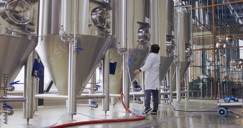 Brewery worker in work process. Man dressed in lab coat at brewery factory near beer tanks