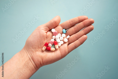 Colorful pills and capsules in a person's hand on a blue background
