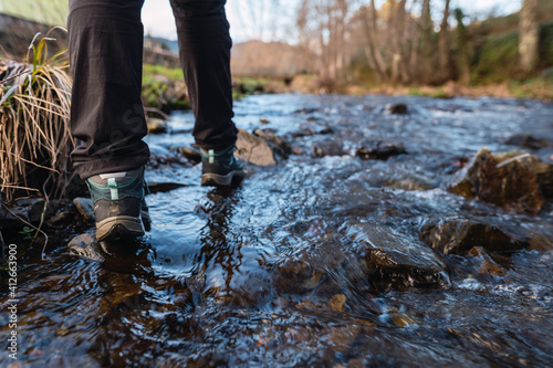 Detail picture of women's hiking boots crossing a river with the water flowing around them.