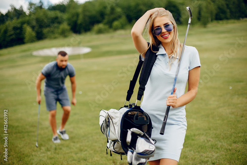 Couple in a golf course. Blonde in a sport clothes. Pair playing golf