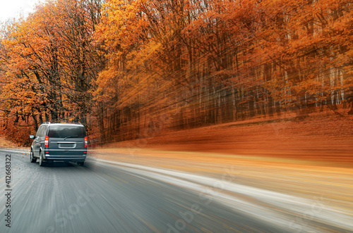 Car is driving along the road against the background of the autumn forest. Blur effect.