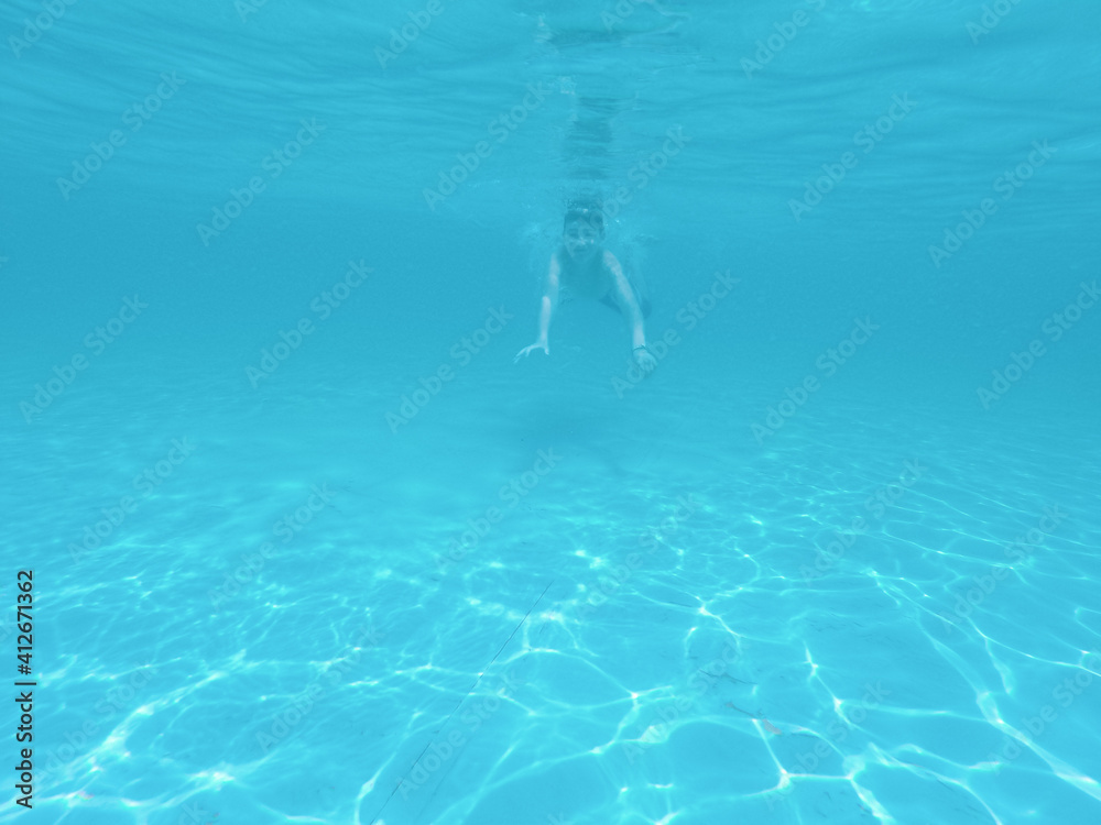 Boy swimming under blue water in pool