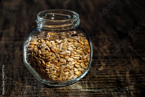 Sunflower seeds in a glass transparent jar. Nuts on an old shabby board. Jar on a brown wooden table close up. Dramatic contrasting light as an artistic effect. photo