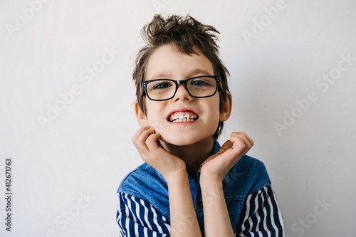 Foto Portrait of autistic boy with glasses in blue shirt on a white backdrop smiling and grimaces