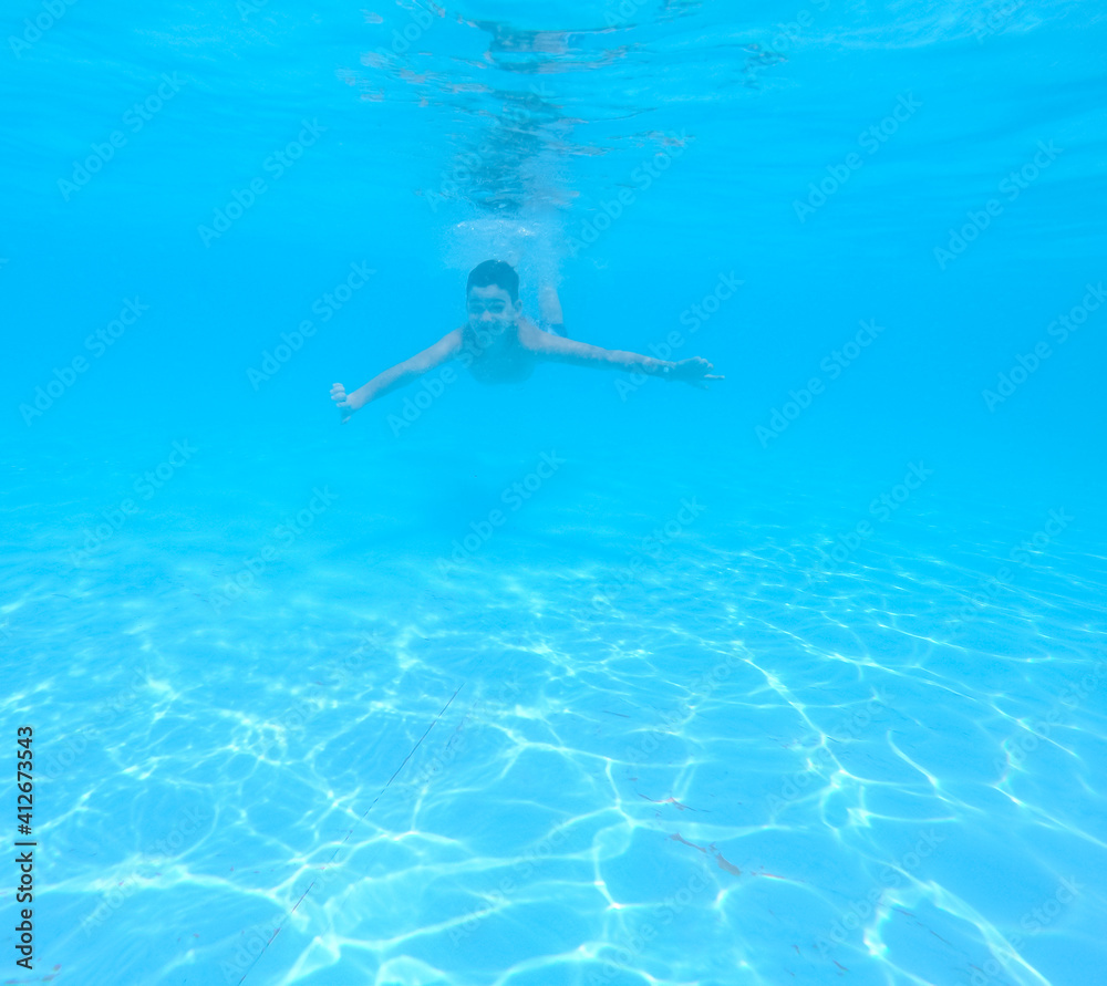 Boy swimming under blue water in pool