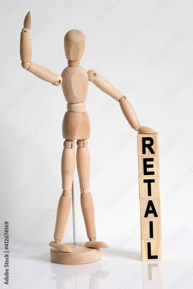 The wooden man raised his hand, and under his left hand he has cubes with the inscription - RETAIL The wooden man raised his hand, and under his left hand he has cubes with the inscription - RETAIL
