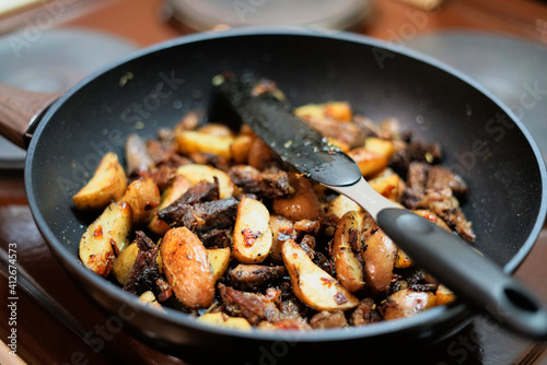 Frying pan with fried golden potatoes and pieces of pork with lots of spices.