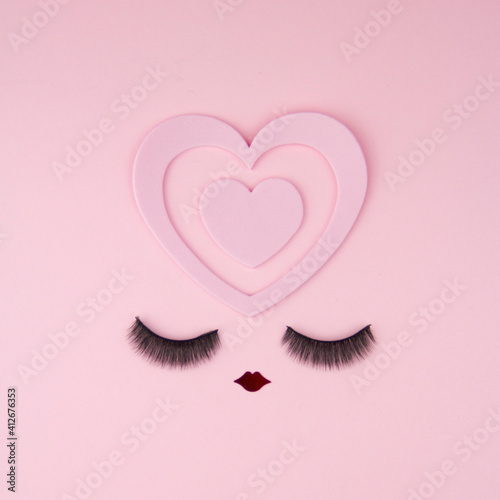 Happy Valentines Day concept of cute face on pink background - artificial face big eyelashes  small red lips and pink heart in mind photo