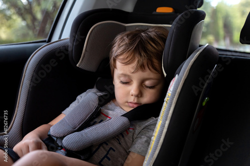Little boy sleeping on the harness booster seat into a car. Security seat for children.
