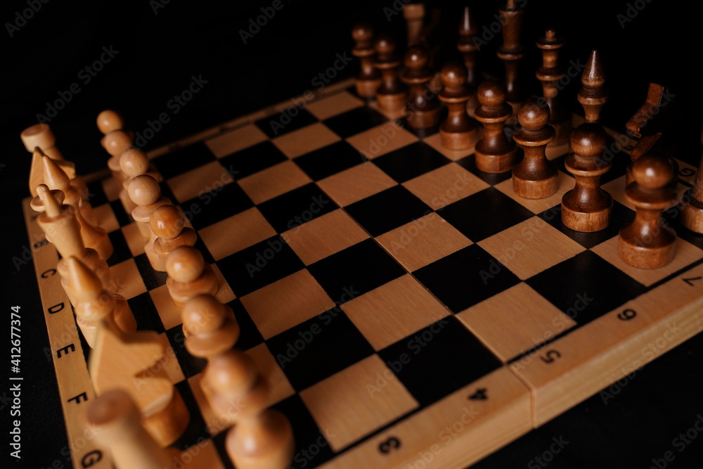 Close up of black chess pieces on board. Two rows of wooden figures on chessboard on black background. Concept of intelligent, logical and strategic game Close up of black chess pieces on board. Two rows of wooden figures on chessboard on black background. Concept of intelligent, logical and strategic game