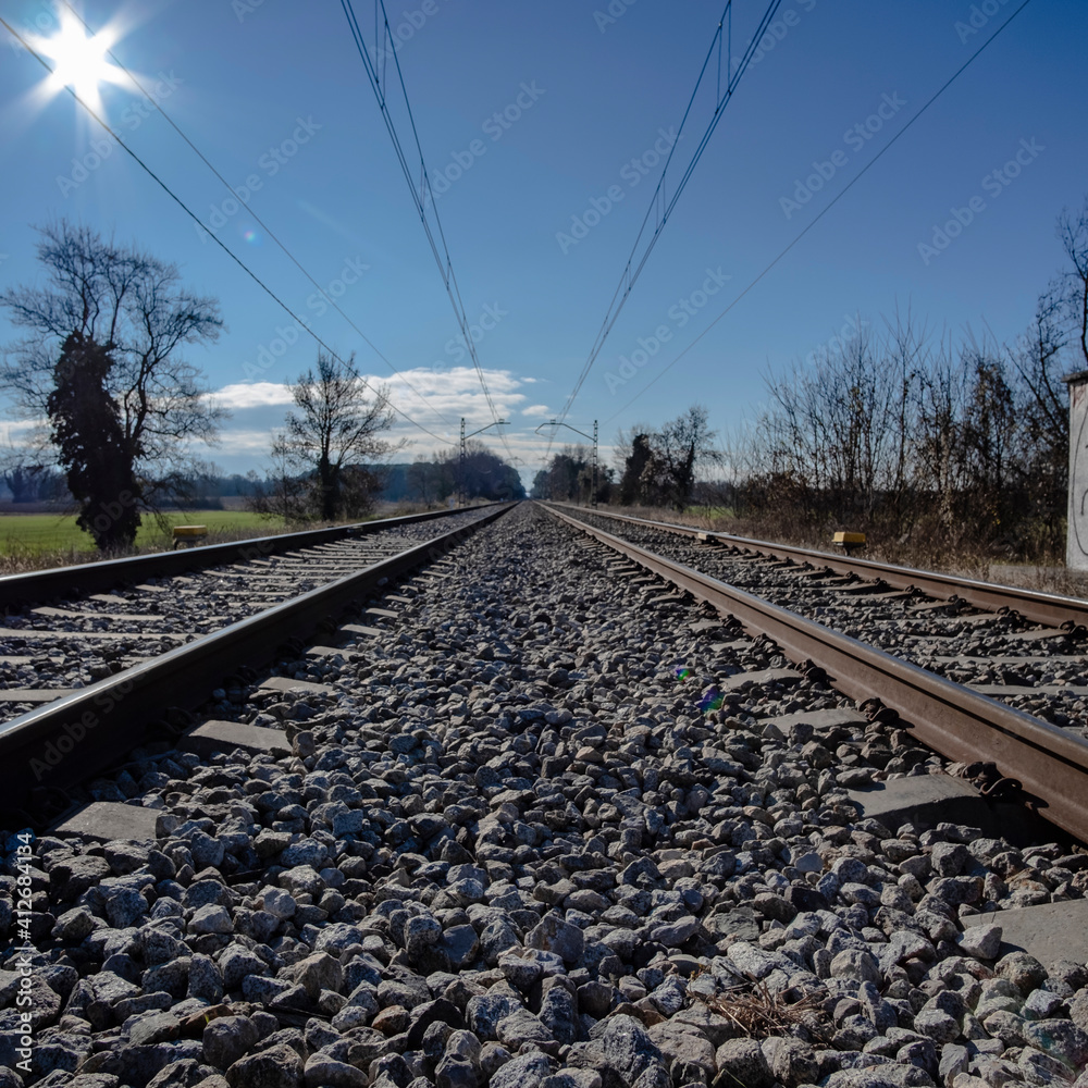 Fototapeta premium Straight railway track perspective over stones on a solid blue sunny sky