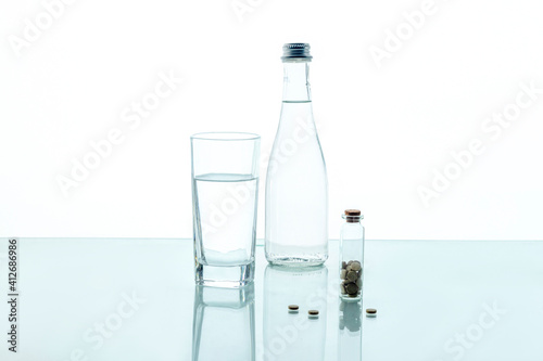 Pills in a transparent jar with a glass of water and a glass bottle on a white background. Medical concept.