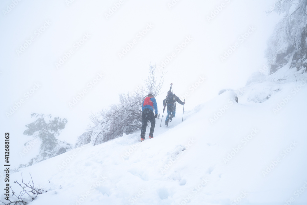 IMAGE OF TWO SKIERS HIKING IN EXTREME CONDITIONS. ALPINISTS TREKKING IN HARSH WINTER CONDITIONS. COLD AND BAD WEATHER CONCEPT.