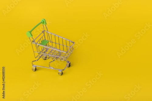 Shopping cart on trendy illuminating yellow color background.