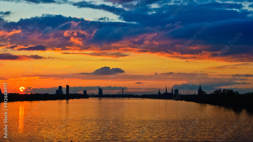 sunset. in the photo, the clouds are illuminated by the evening sun,in the foreground is a river, in the background is a city