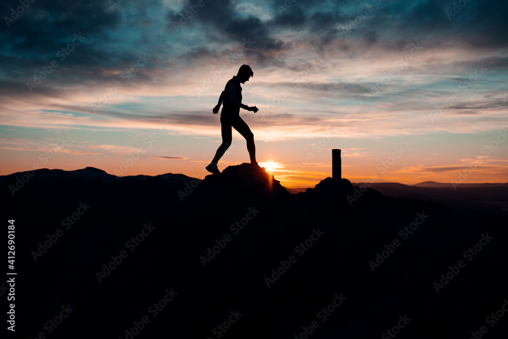 PERSON JUMPING AT THE TOP OF A MOUNTAIN. MAN ENJOYING AND HAVING FUN DURING SUNSET. OUTDOOR AND SUNSET CONCEPT.