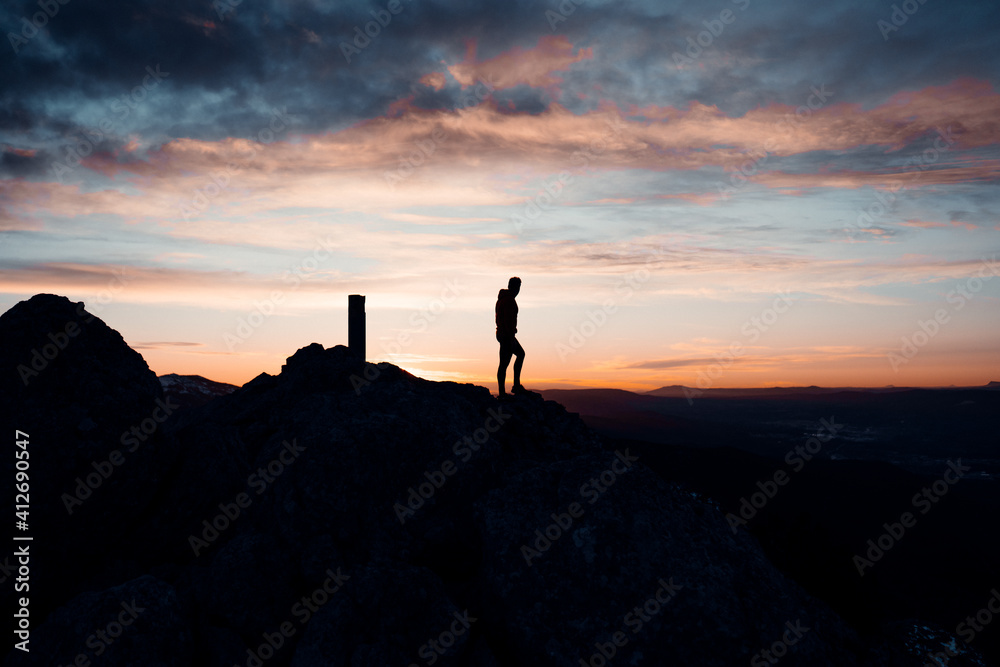 IMAGE OF A PERSON WALKING AT THE TOP OF A MOUNTAIN. MAN ENJOYING AND HAVING FUN DURING SUNSET. OUTDOOR AND SUNSET CONCEPT.
