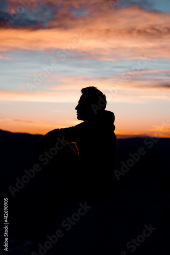 SILHOUETTE OF A PERSON AT THE TOP OF A MOUNTAIN. MAN RELAXING AND MEDITATING DURING SUNSET. OUTDOOR AND SUNSET CONCEPT.