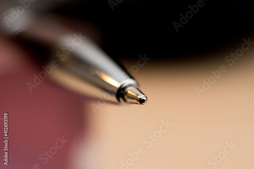 Macro close-up of tip of a shiny metallic ballpoint pen with burred background.