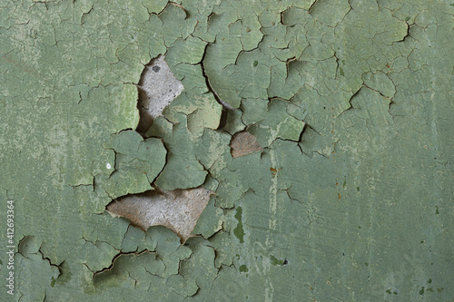 Green peeling paint on the wall. Old concrete wall with cracked flaking paint. Weathered rough painted surface with patterns of cracks and peeling. High resolution texture for background and design.