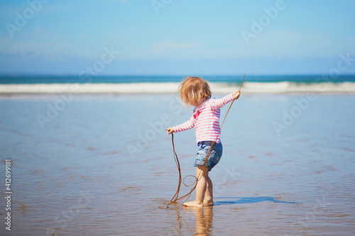 Fotografia Adorable toddler girl playing with weeds on the sand beach at Atlantic coast of