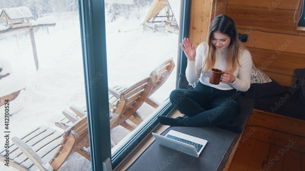 Young caucasian woman drinking coffee and using laptop near the window in winter. High quality photo