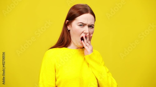 Slim redhead woman yawning at yellow background. Portrait of tired or bored beautiful Caucasian lady. Exhaustion and boredom concept. Slow motion. photo