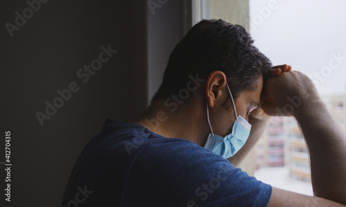 Tired man in medical mask looks out the window.
