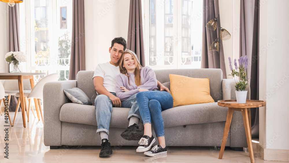 Portrait of young couple smiling and looking at the camera while sitting on the couch at home. Portrait of young couple smiling and looking at the camera while sitting on the couch at home.