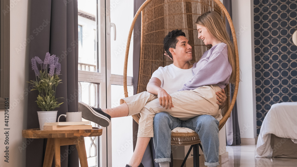 Portrait of young couple looking at each other while sitting in a wicker chair together at home. Portrait of young couple looking at each other while sitting in a wicker chair together at home.