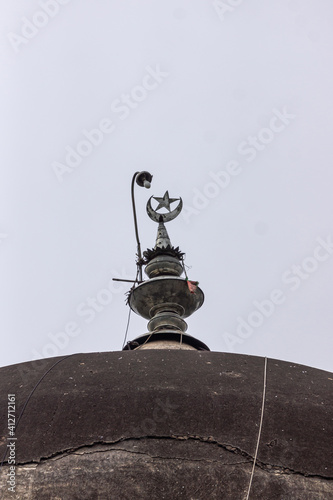 Vijayapura, Karnataka, India - November 8, 2013: Jod Gumbaj Tombs. Closeup of crescent moon statue with lamp on top of dome under silver sky. photo