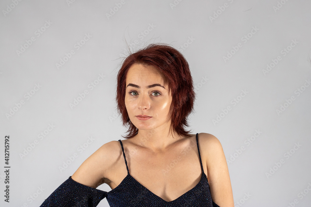 A young female attractive caucasian model with album red hair in a studio with a white background wearing a black dress. A young female attractive caucasian model with album red hair in a studio with a white background wearing a black dress.