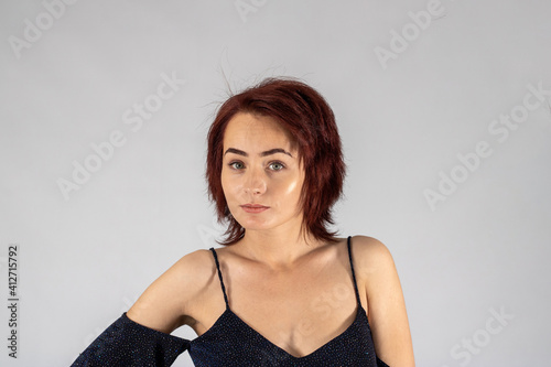 A young female attractive caucasian model with album red hair in a studio with a white background wearing a black dress.