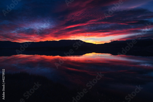 Sunrise or sunset with purple and red clouds reflected in the lake water. Natural mirror at blue hour. Spectacular and beautiful scenery. Estany de Banyoles, Girona, Catalonia, Spain.