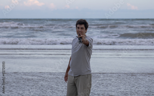 Brunette man on the beach with a happy expression and holiday mood with waves in the background and clouds passing in Santa Catarina, Brazil. A late afternoon sky in a tropical paradise.