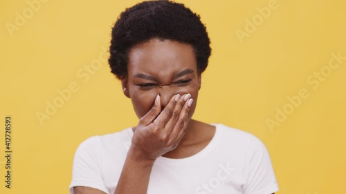 Close up portrait of young displeased african american woman smelling stinky odor, closing her nose, orange background