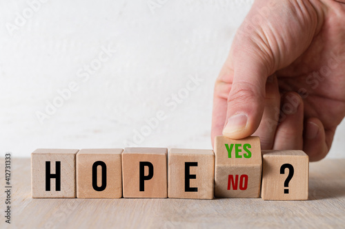 hand turning a cube with text YES and NO answering the question HOPE? on wooden background